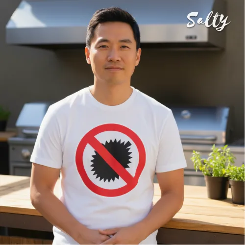 Singapore streetwear — person outdoors at patio grill station wearing Wetteeshirt x Salty white graphic t-shirt with bold red prohibition circle over black saw blade icon, casual lifestyle fashion shot with wooden counter and potted plants in backyard setting.