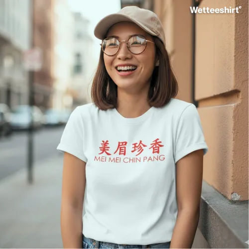 Smiling person in beige cap and glasses on city street wearing white Wetteeshirt® tee with bold red Chinese characters ‘美眉珍香’ and romanized text ‘MEI MEI CHIN PANG’, casual unisex Singapore streetwear fashion.