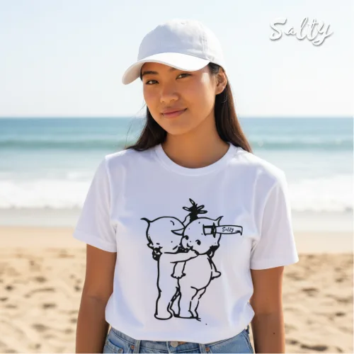 Singapore streetwear — person on sandy beach wearing Wetteeshirt® X Salty white graphic t-shirt with playful black line art of two cartoon characters, one holding device labeled ‘RELAX’ to other’s head, styled with white baseball cap, lifestyle fashion shot with ocean and sky backdrop.