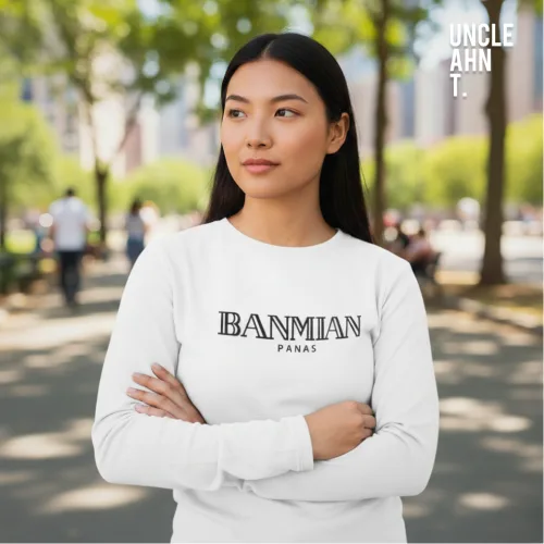 Outdoor lifestyle photo of a man in a white long‑sleeve graphic tee with bold black text ‘BANMIAN PANAS,’ standing on a sunlit park pathway surrounded by trees, part of Wet Tee Shirt® x Uncle Ahn T Singapore streetwear collection.