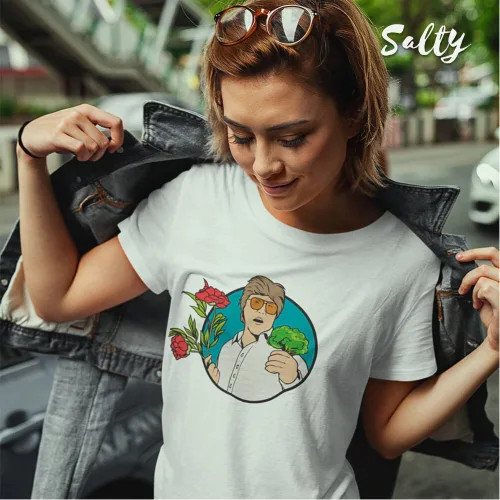 Singapore streetwear — person outdoors revealing Wetteeshirt® x Salty white graphic t-shirt under denim jacket, featuring cartoon character with sunglasses holding drink and herbs, surrounded by red flowers and green leaves on bold blue circular background, trendy lifestyle fashion shot.
