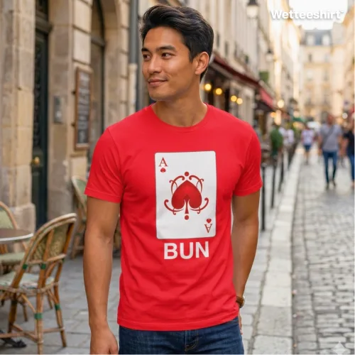 Person on cobblestone street in European‑style city wearing bright red Wetteeshirt® Bun (Ace) tee with stylized Ace of Spades card design resembling a bun pastry and bold white ‘BUN’ text, playful unisex streetwear fashion.jpg