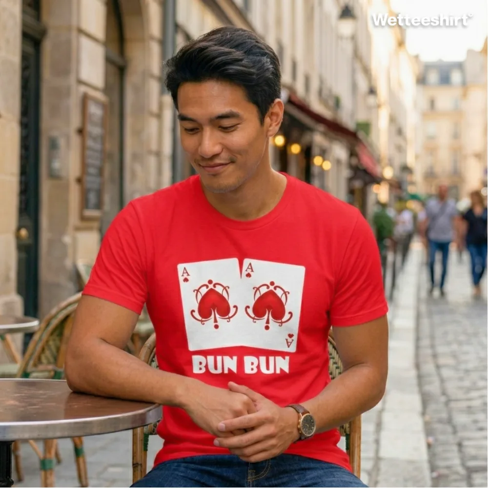 Person at outdoor café table in European‑style city wearing bright red Wetteeshirt® Bun Bun tee with playful double Ace of Spades card design featuring red bunny illustrations and bold white ‘BUN BUN’ text, quirky unisex streetwear fashion.jpg