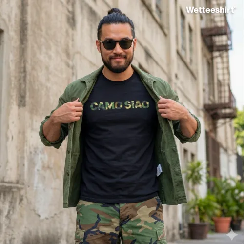Man in urban setting wearing sunglasses, green military jacket, and camouflage pants with black Wetteeshirt® Camo Siao tee featuring bold camouflage text design, edgy unisex streetwear inspired by military humor.jpg