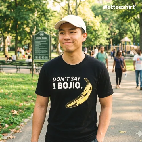 "Person in white cap wearing black ‘DON’T SAY I BOJIO’ T-shirt with yellow banana graphic, casual unisex streetwear by Wetteeshirt, Singlish slang fashion statement, premium cotton tee, playful Singapore cultural apparel, trendy urban outfit for men and women.