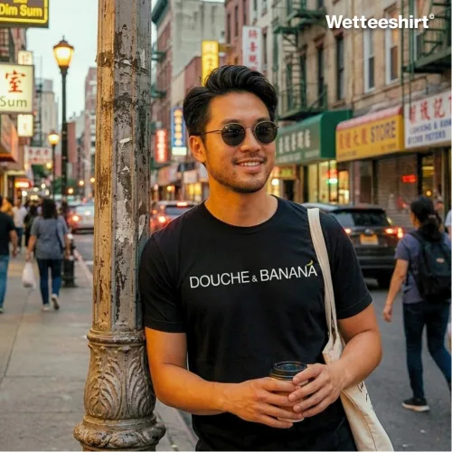 Man in sunglasses wearing black ‘DOUCHE & BANANA’ T-shirt, holding drink and tote bag on busy Chinatown street, casual unisex streetwear by Wetteeshirt®, premium cotton tee with humorous bold design, trendy urban fashion outfit for men and women, Singapore cultural apparel.