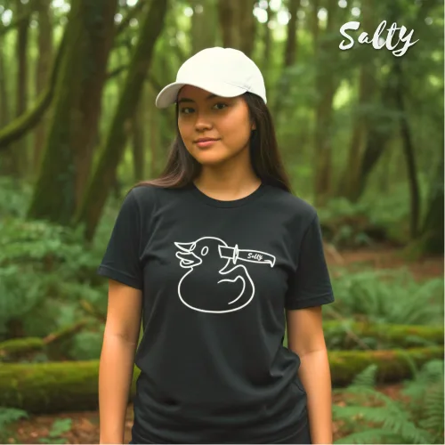Singapore streetwear — person in forest wearing Wetteeshirt® X Salty black graphic t-shirt with bold duck illustration stabbed by knife labeled ‘SALTY,’ styled with white cap, lifestyle fashion shot with tall trees and sunlight background.