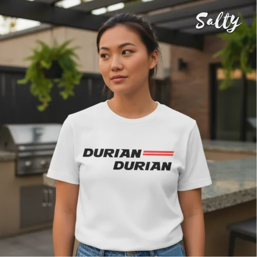 Singapore streetwear — person outdoors in modern patio wearing Wetteeshirt® X Salty white graphic t-shirt with bold black ‘DURIAN DURIAN’ text and three red horizontal lines, casual lifestyle fashion shot with grill, countertop, and hanging plants in stylish backyard setting.
