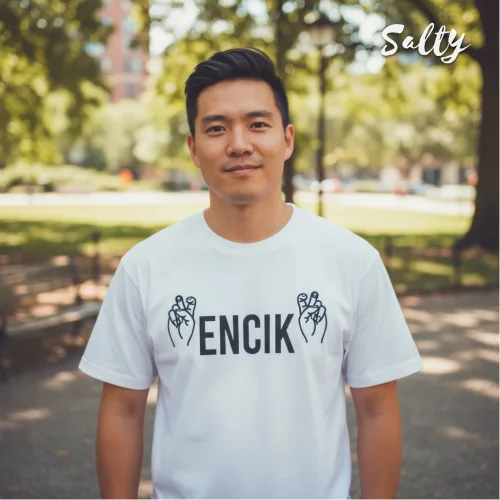 Singapore streetwear — man outdoors in park wearing Wetteeshirt® X Salty white graphic t-shirt with bold black ‘ENCIK’ text flanked by two hand gesture illustrations, casual lifestyle fashion shot with trees and benches in background.