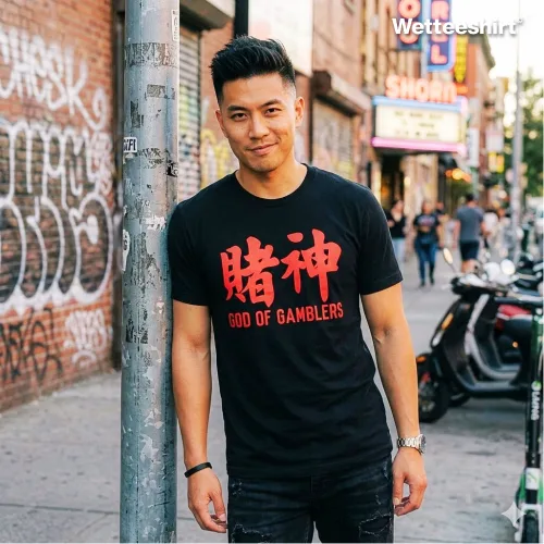 Urban streetwear photo of a man wearing the Wet Tee Shirt 赌神 God of Gamblers black graphic T‑shirt with bold red Chinese characters and English text, standing on a graffiti‑covered city sidewalk with neon storefront and stickered pole — edgy Asian street style casual tee for men.