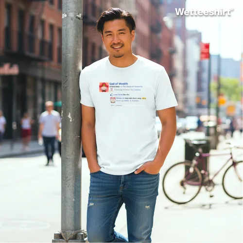 Streetwear fashion photo of a man wearing the Wet Tee Shirt God of Wealth white graphic T‑shirt with social media meme design featuring playful text and money emojis, paired with blue jeans, standing on a city street with pedestrians, bicycle, and urban buildings — trendy casual Asian street style meme tee for men.