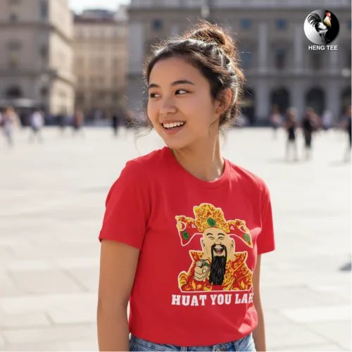 Unisex red short sleeve T-shirt with colorful cartoon deity holding gold ingots and bold “HUAT YOU LAH” slogan, festive Singapore streetwear by Wet Tee Shirt®