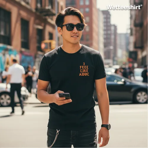 Black streetwear T-shirt with bold orange ‘I FEEL LIKE AWOL’ slogan, styled with sunglasses and smartphone in hand, worn on a busy city street with urban buildings and pedestrians — trendy hip-hop inspired fashion for men.
