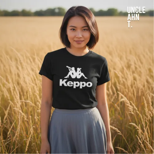 Singapore streetwear Keppo black short sleeve T-shirt, white logo of two seated figures with bold text below, casual unisex tee by Uncle Ahn T, premium cotton playful design photographed outdoors in golden grass