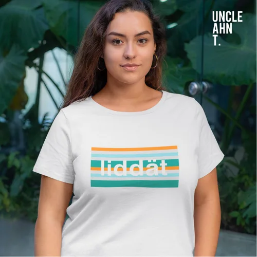 Singapore streetwear liddat white short sleeve T-shirt, colorful teal‑orange‑white striped rectangle with lowercase text, casual unisex tee by Uncle Ahn T, premium cotton playful design photographed outdoors with tropical leaves