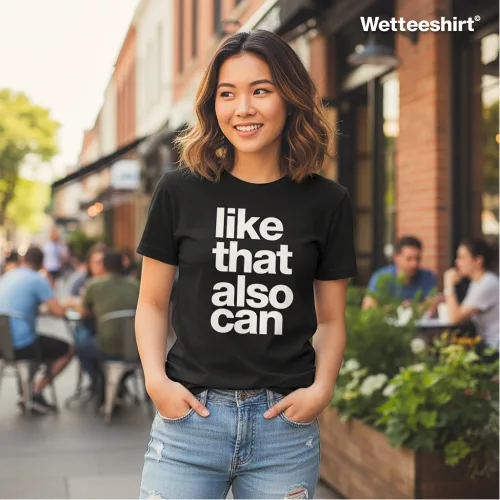 Black casual T-shirt with bold white ‘like that also can’ slogan, styled with ripped blue jeans and hands in pockets, worn outdoors in lively street café setting with people dining — witty streetwear fashion inspired by playful Singlish humor.