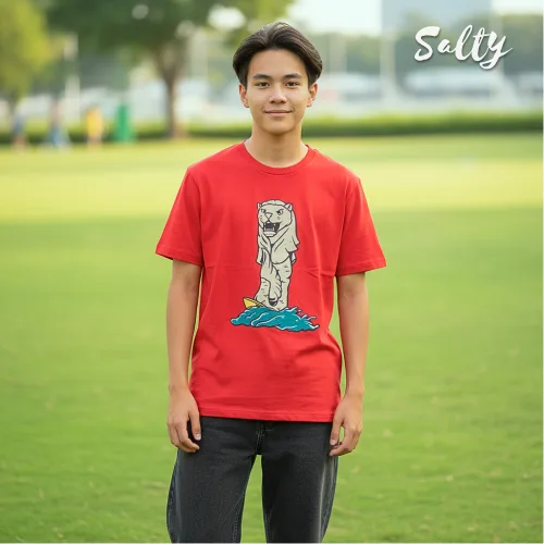 "Singapore streetwear — person in park wearing Wetteeshirt® x Sally red graphic t-shirt featuring upright fish illustration rising from blue waves, casual outdoor lifestyle fashion shot with grassy field and trees in background.