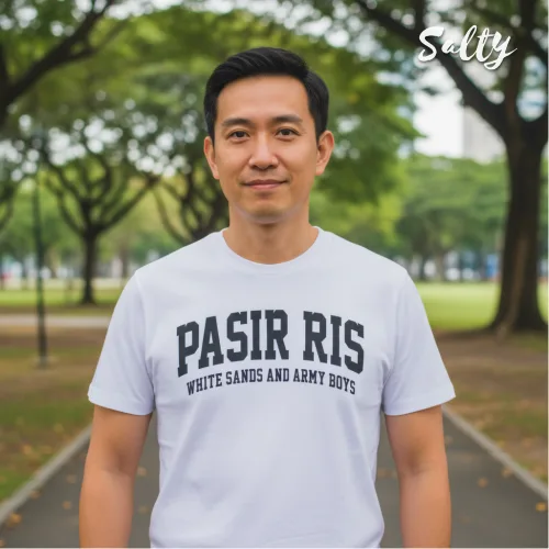 Singapore streetwear — man outdoors on park pathway wearing Wetteeshirt® × Solly white graphic t-shirt with bold black text ‘PASIR RIS WHITE SANDS AND ARMY BOYS,’ casual lifestyle fashion shot with trees and greenery in background.