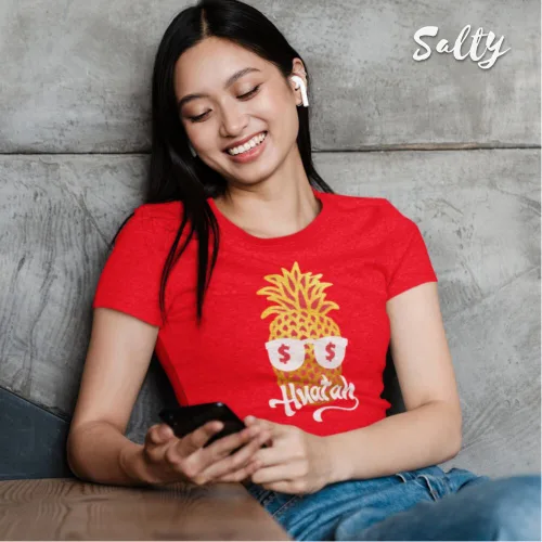 Singapore streetwear — person indoors on couch smiling at smartphone, wearing Wetteeshirt™ × Selly red graphic t-shirt with playful pineapple in sunglasses featuring dollar sign lenses and stylized ‘Hwat ah’ text, casual lifestyle fashion shot with earbuds and relaxed vibe.