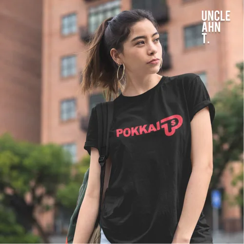 Singapore streetwear POKKAI black short sleeve T-shirt, bold red letters with stylized logo graphic, casual unisex tee by Uncle Ahn T, premium cotton playful design photographed outdoors with urban backdrop