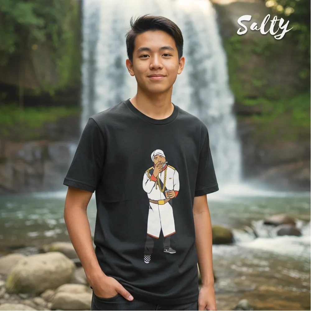 Singapore streetwear — young person outdoors at waterfall wearing Wetteeshirt × Salty black t-shirt featuring Salt Bae meme graphic of man sprinkling salt in white outfit, lifestyle fashion shot with lush greenery and rocks in background.
