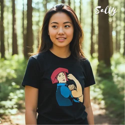 Singapore streetwear — person in forest wearing Wetteeshirt® x Solly black graphic t-shirt inspired by ‘We Can Do It!’ poster, featuring stylized character with red headscarf flexing arm, lifestyle fashion shot with tall trees and sunlight background.
