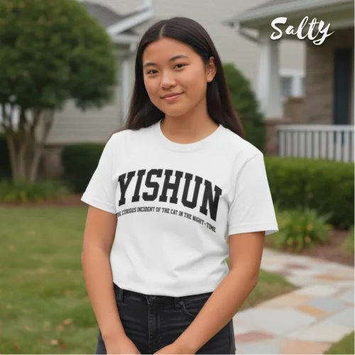 "Singapore streetwear — young person outdoors in residential neighborhood wearing Wetteeshirt® X Salty white graphic t-shirt with bold black text ‘YISHUN THE STRONG MEMORY OF THAT CAT IN THE STREET, STRONG,’ casual lifestyle fashion shot with house, bushes, and walkway in background.